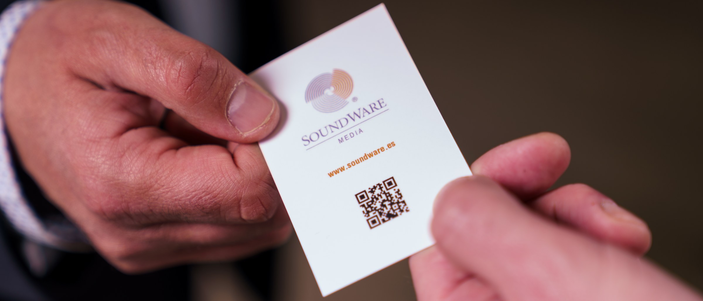 Dos manos intercambiando una tarjeta de visita de Soundware Media